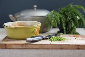 A pot, a bowl, a knife and some chopped chives on a cutting board